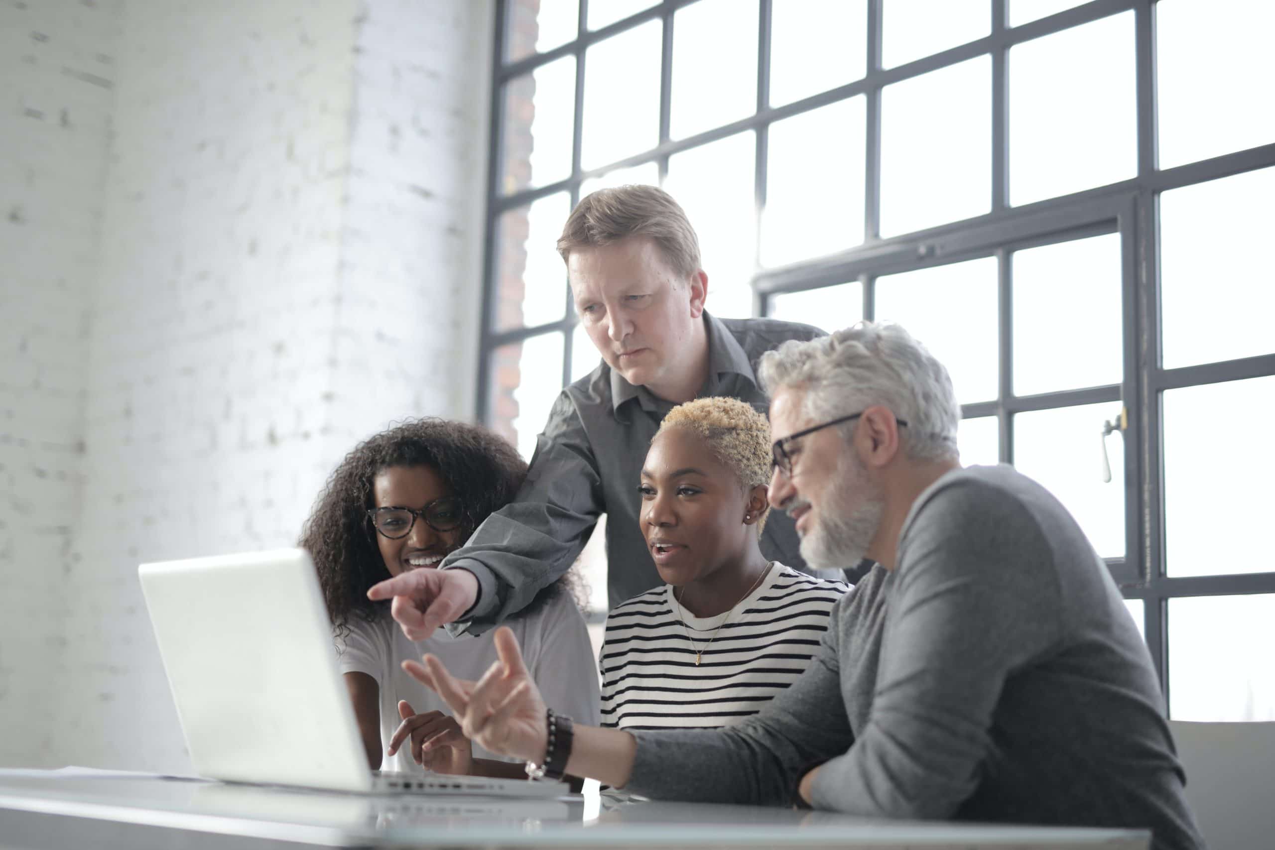 Four people pointing at a laptop screen.